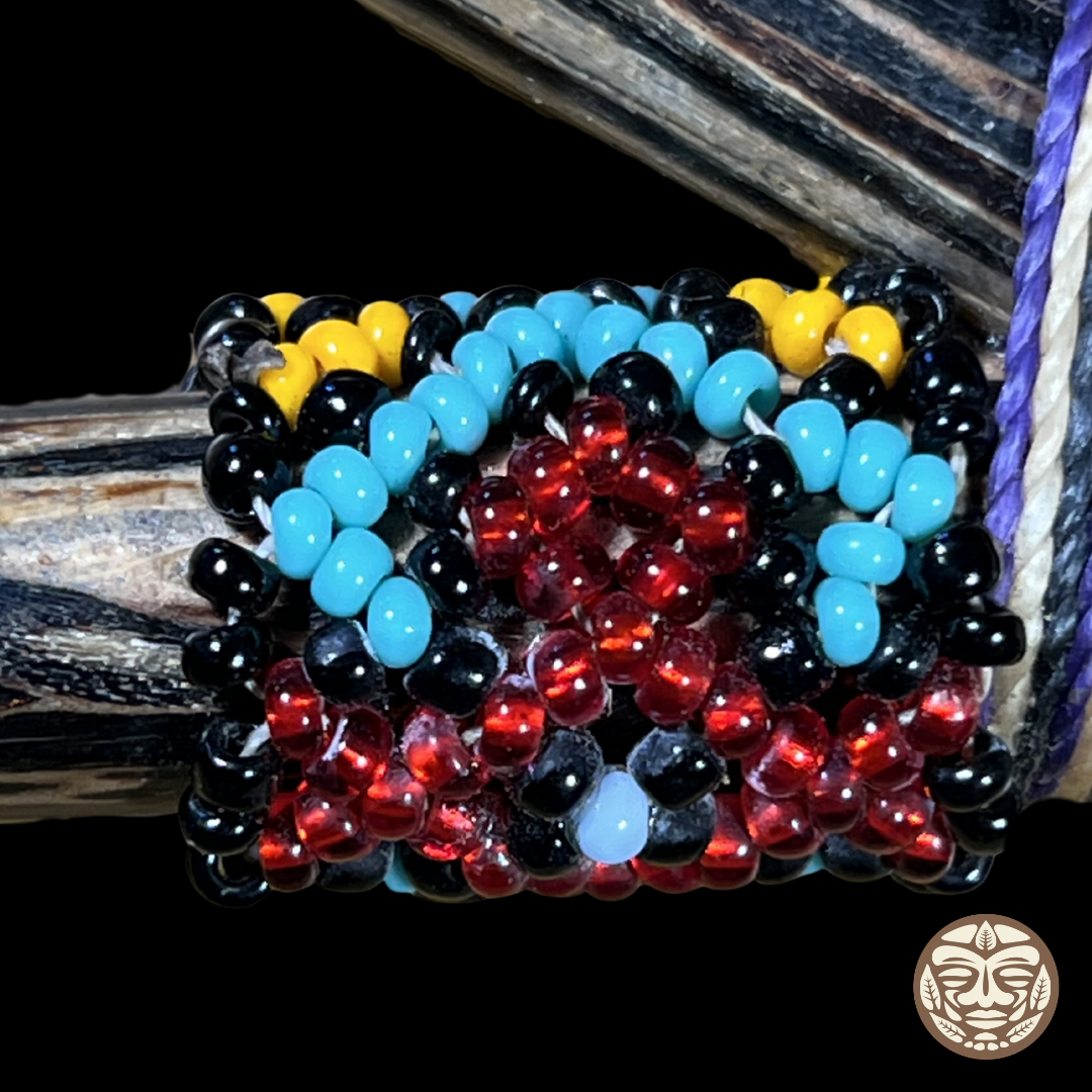 A close-up of a beaded kruipe, featuring rows of glossy black, bright turquoise blue, translucent red, and yellow beads, displayed on a dark palo chonta wood.