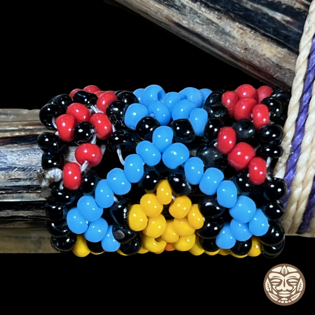 A close-up of a beaded wrap kuripe featuring rows of glossy black, light blue, red, and yellow beads, shown wrapped around a dark palo chonta wood.