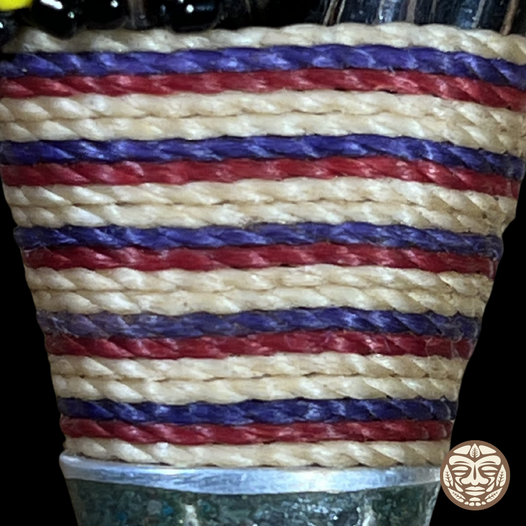 A close-up of a kuripe wrapped with horizontal braided rope stripes in natural beige, red, and purple, with a dark base.