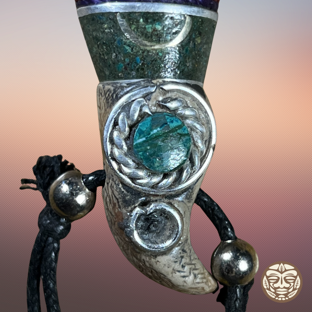 A close-up of a carved turquoise and silver ceremonial dagger or spear tip, featuring a central turquoise stone, a textured green stone body, and black cord with silver beads.