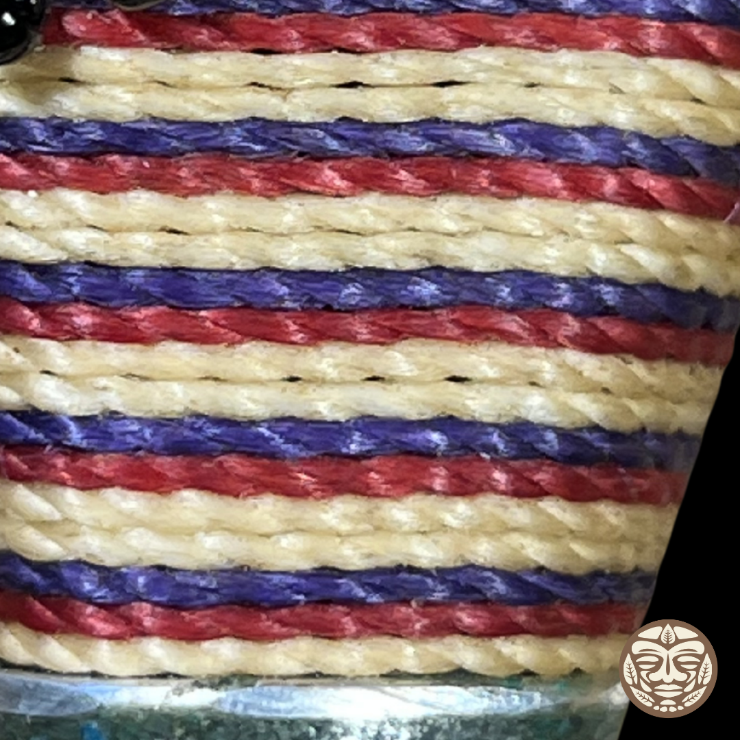 Close-up of a braided chambira rope with horizontal stripes in cream, red, and purple, photographed tightly against a dark background.