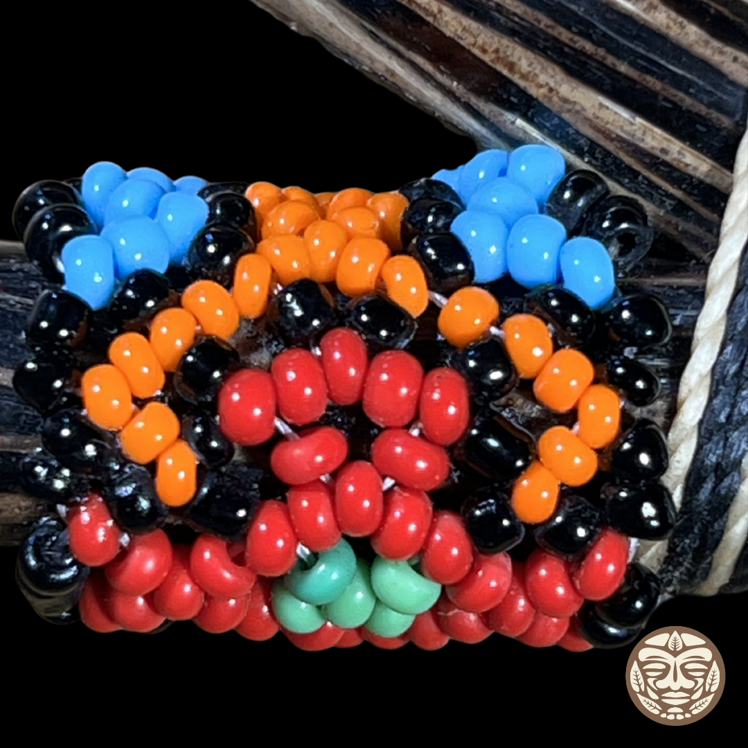 A close-up of a handmade beaded kuripe featuring multiple rows of glossy, oval-shaped beads in bright blue, orange, red, black, and mint green.