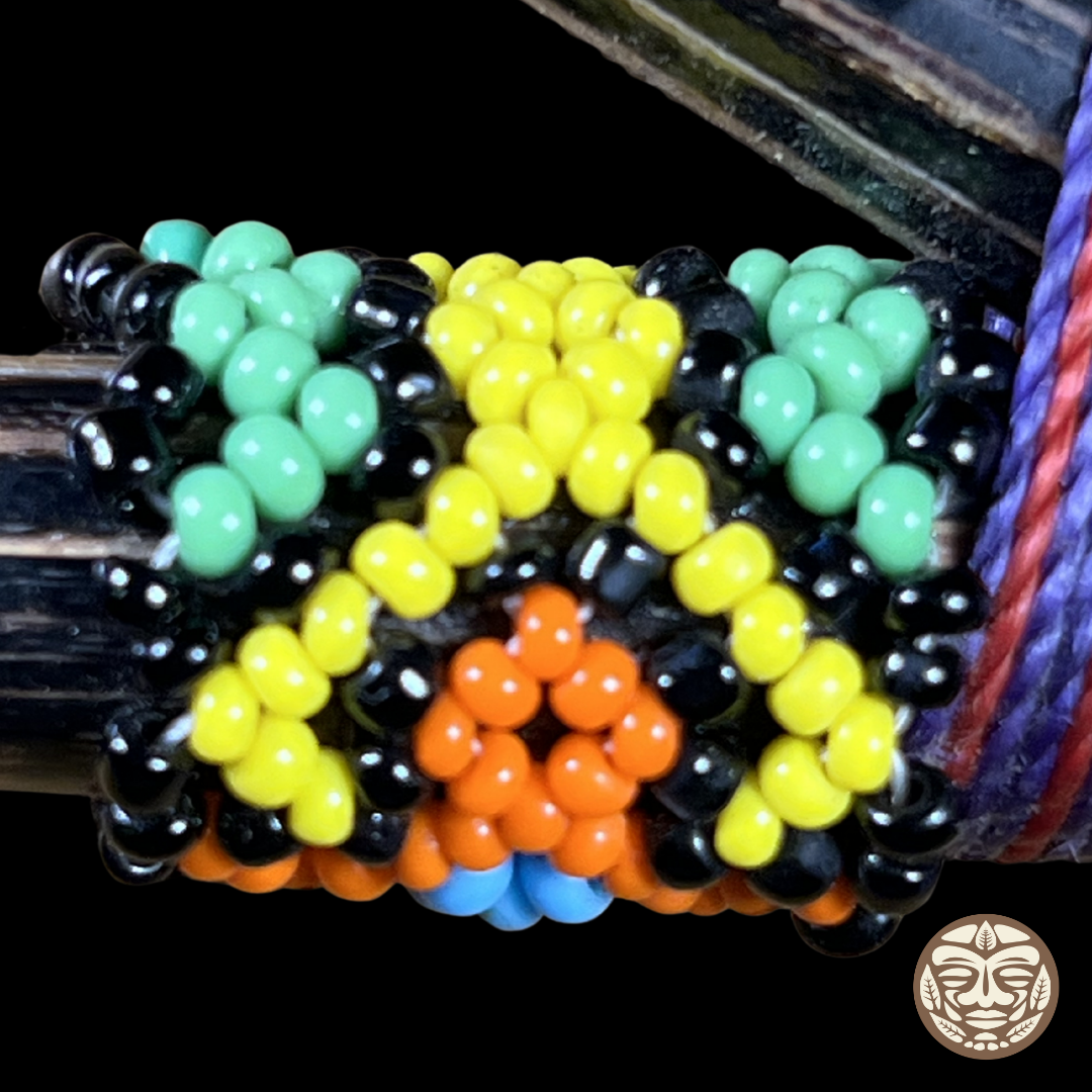 A close-up of a beaded wrap kuripe with a pattern of mint green, yellow, black, orange, and light blue beads, shown wrapped around a dark wood.