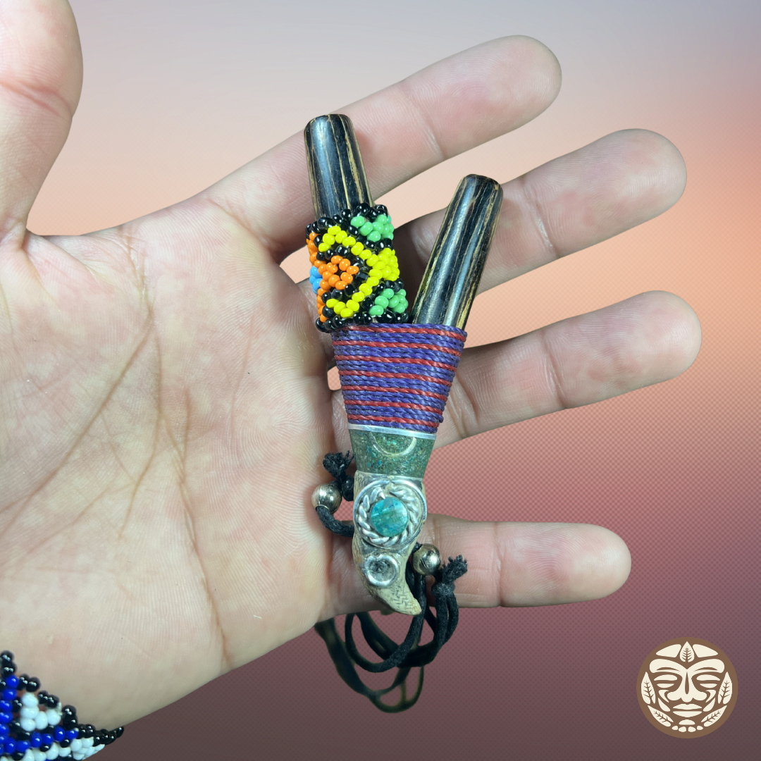 A hand holding a palo chonta kuripe made wrapped with red and blue cord, decorated with a colorful beadwork pattern, and a turquoise stone at the clasp.