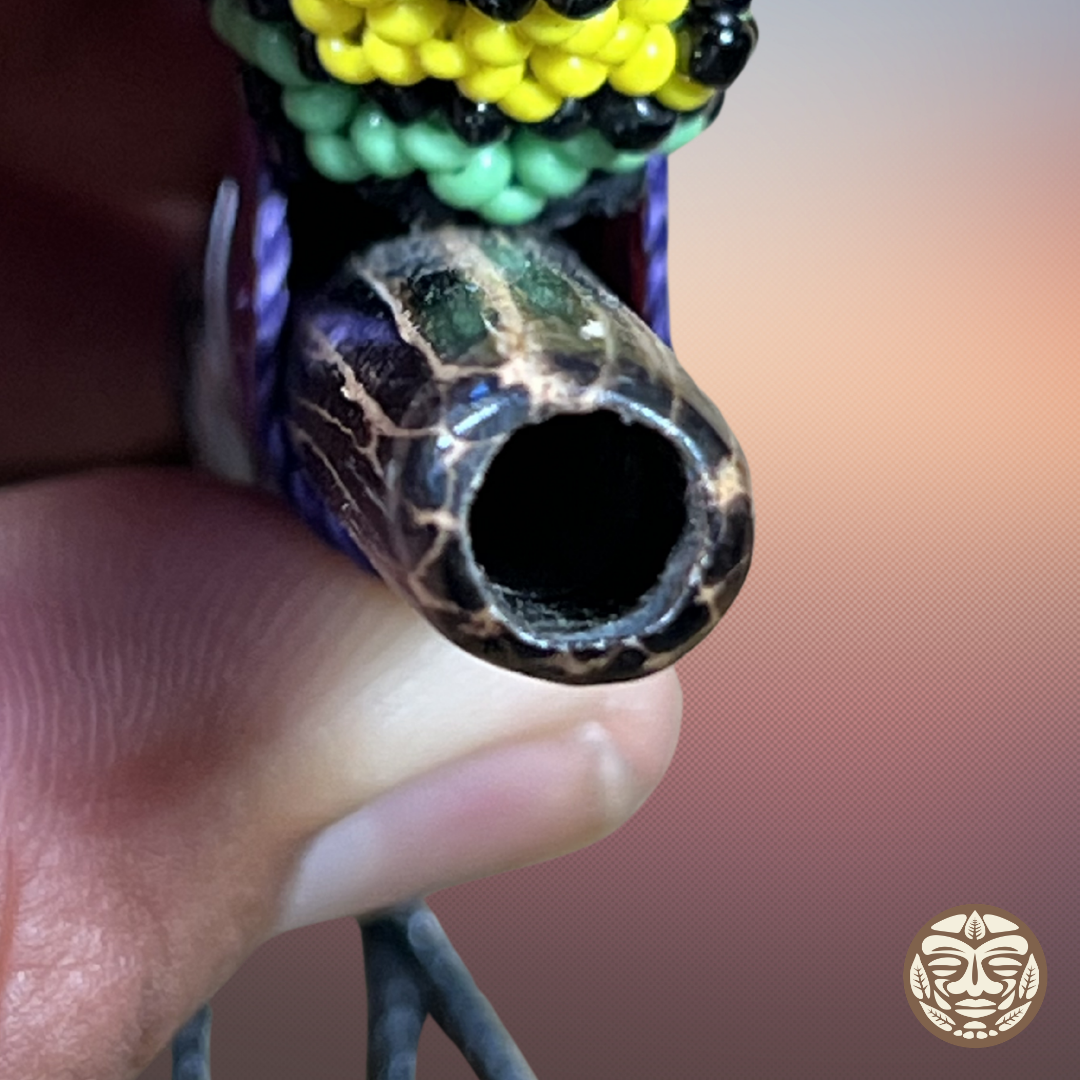 A close-up of a hand holding a decorative beaded kuripe mouth hole with a glossy black and gold marbled pattern. 