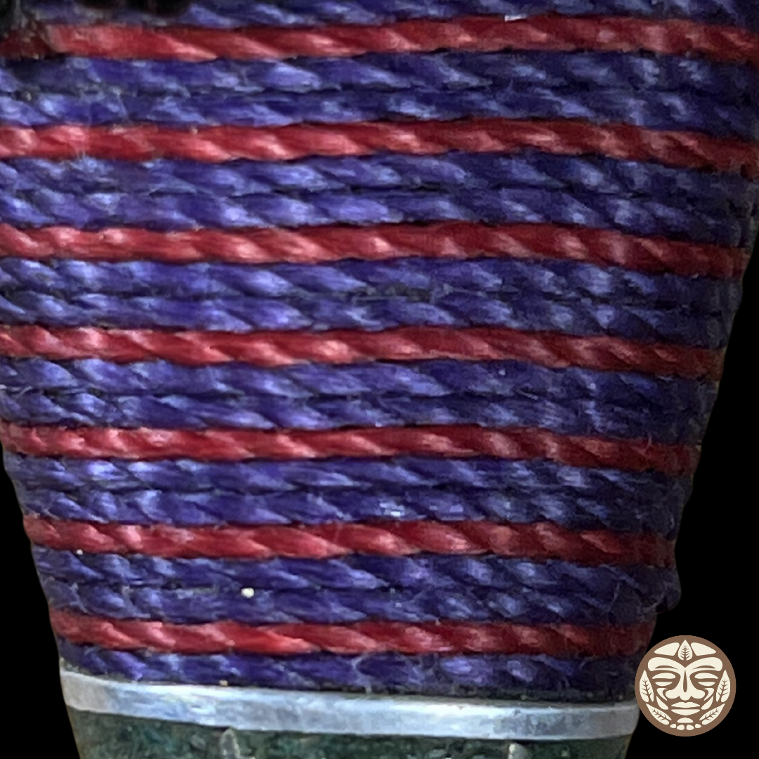 A close-up of a woven textile or strap wrapped around a cylindrical form, showing alternating horizontal stripes of purple and red thread.